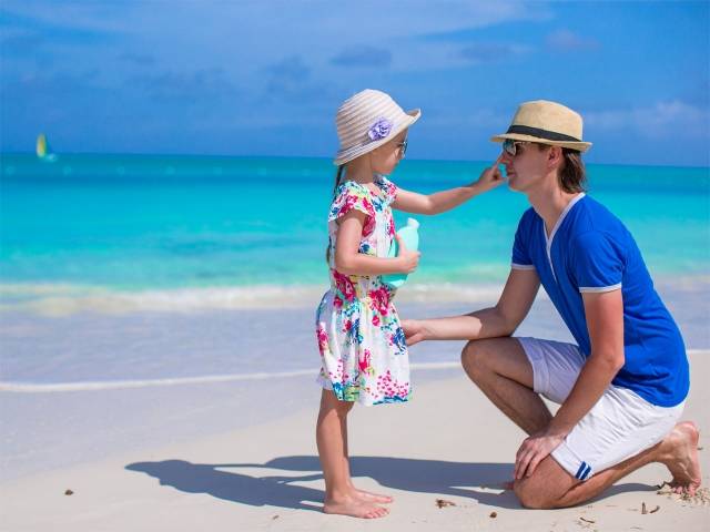 Niña aplicando crema solar a su padre en la playa
